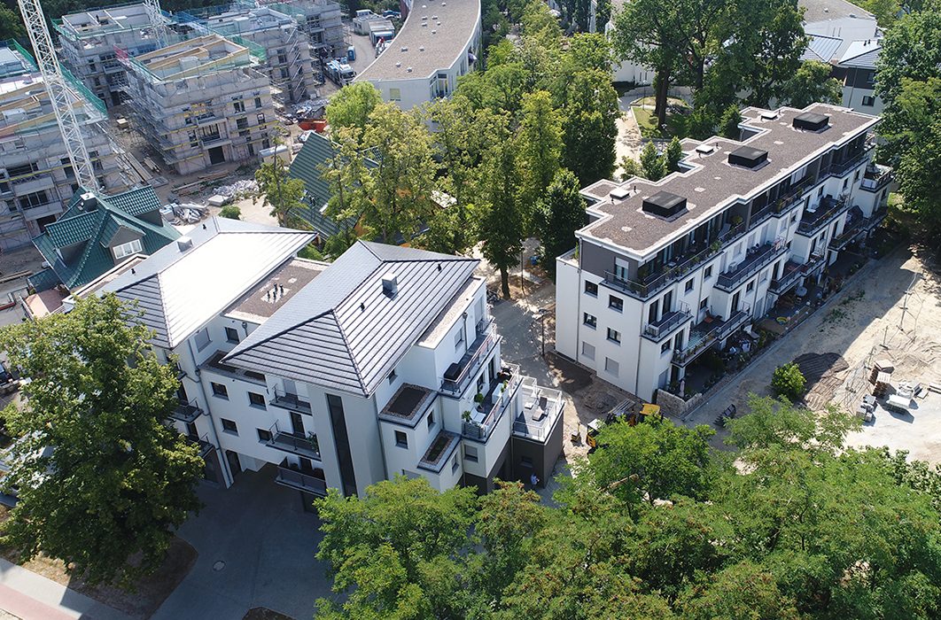 Luftaufnahme moderner weißer Mehrfamilienhäuser im Allee-Quartier Teltow zwischen alten Bäumen