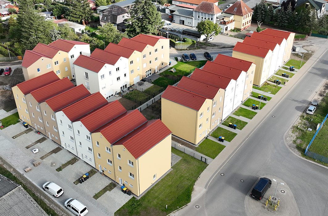Luftaufnahme der Reihenhaus-Wohnanlage Zur Mesche mit gelben Fassaden und roten Ziegeldächern